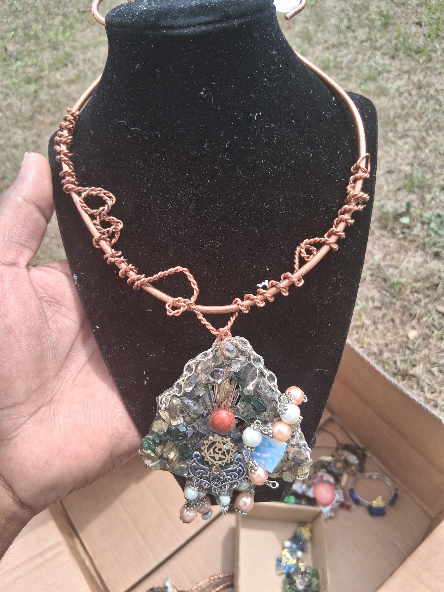 Copper necklace with a crystal and glass pendant displayed on a stand